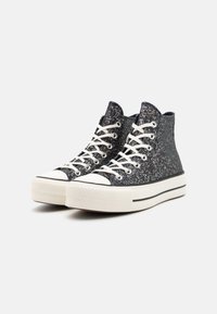 Höga sneakers i svart glittermaterial med vita snören, gummikappa på tån och tjock vit sula med en svart rand.