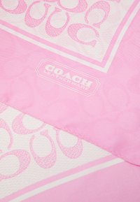 Rosa stof med gentagende "C" mønster og hvid "Coach Leatherware" logo i midten.