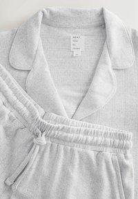 Lichtgrijze pyjama-set met een collared top en broeken met een elastische tailleband. De textuur van de stof heeft subtiele verticale strepen en kleine stippenpatronen.