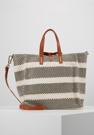 Large woven tote bag with black and white diagonal stripes, tan leather handles, and an adjustable shoulder strap, resting on a white pedestal.