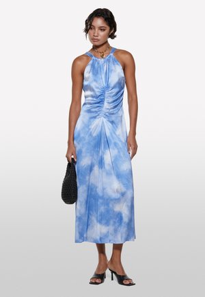 Robe midi bleu tie-dye avec un décolleté halter, un corsage froncé et des plis à l'avant ; accompagnée d'un sac à main en osier noir et de sandales à talons noires.
