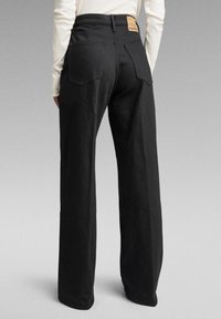 Svarta vida byxor med hög midja, med en lädermärke på baksidan och enkla fickdetaljer. Strukturerad tygfinish.