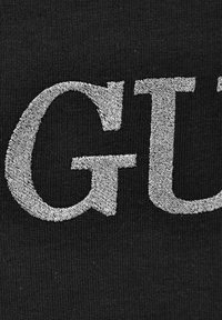 Svart tyg med stora, strukturerade silverbokstäver med en svag glans, som betonar fet typografi mot en enkel bakgrund.