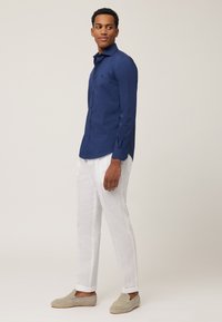 Navyblaues Langarmhemd mit tailliertem Design, Button-Down-Kragen, kombiniert mit weißen Leinenhosen und beigen Loafers.