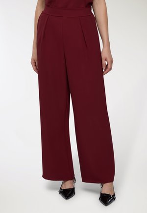 Pantaloni ampi bordeaux con vita alta, caratterizzati da pince e una texture liscia, abbinati a tacchi a punta neri.