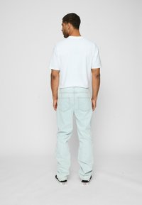 Blugi de denim de culoare albastră deschisă, cu o croială lejeră, având buzunare la spate, purtați cu un tricou alb simplu și adidași negri.