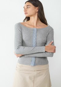 Gray long-sleeve shirt with a ribbed texture, boat neckline, and light blue button placket down the front. Worn with a beige skirt.