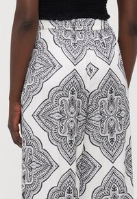 Pantalones de patrón blanco y negro con una cintura elástica, que presentan intrincados diseños paisley y una textura de tela suave.