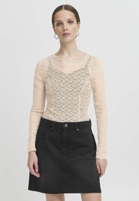 Top in pizzo a maniche lunghe di colore rosa chiaro sovrapposto a una gonna in denim nera. Il top presenta un delicato motivo floreale e un colletto rotondo.
