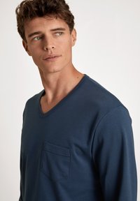 Navy blauwe longsleeve V-hals shirt van gladde stof, met een borstzak en subtiele stikdetails op de rand van de zak.
