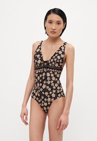Maillot de bain une pièce noir à motif floral avec un décolleté en V profond, des bretelles ajustables étroites et un détail à nouer au centre, orné de motifs floraux beiges.