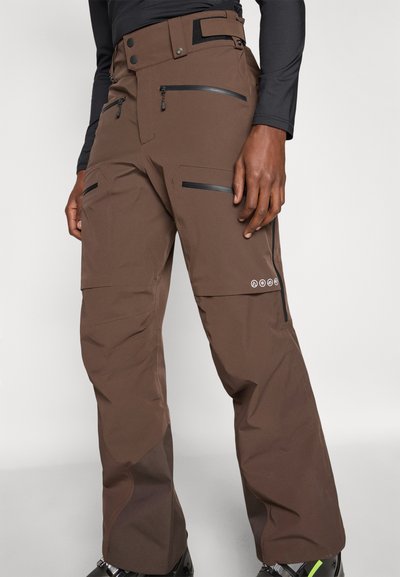 Bruna skidbyxor i slitstarkt tyg, med blixtlåsförsedda fickor, hög midja och svarta detaljer på fickorna och benen.