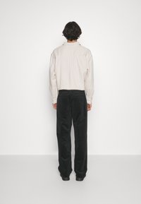 Ljusbeige oversized skjorta med bakstycke och lös passform, i kombination med svarta, vida corduroybukser. Matt yta utan synliga mönster.