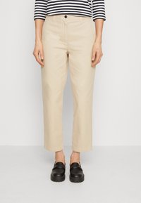 Béžové chinos kalhoty s rovný střihem a manžetovými lemy, spárované s černými koženými slip-on botami. Nosené s pruhovaným dlouhým rukávem.