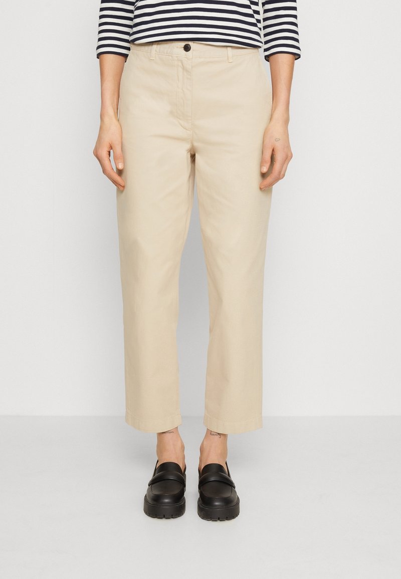 Béžové chinos kalhoty s rovný střihem a manžetovými lemy, spárované s černými koženými slip-on botami. Nosené s pruhovaným dlouhým rukávem.