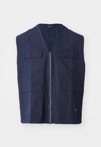 Chaleco sin mangas de color azul marino en algodón con cierre de cremallera, que cuenta con cuatro bolsillos frontales y un diseño de escote en V. Textura suave y detalles mínimos.