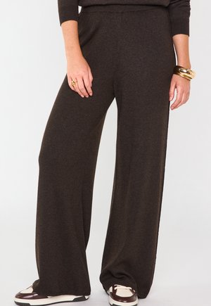 Braune weit geschnittene Hosen aus weichem Stoff mit einem elastischen Bund, kombiniert mit mehrfarbigen Sneakers mit cremefarbenen und burgunderroten Akzenten.