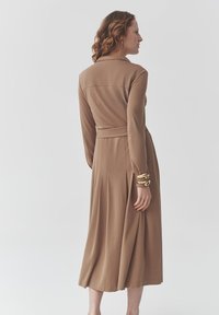 Langes, kastanienbraunes Kleid aus glattem Stoff mit Kragen, langen Ärmeln, tailliertem Bund und gefälteltem Rockdetail hinten.