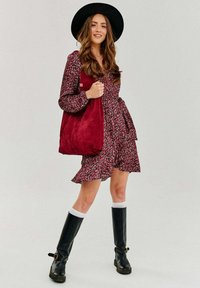 Kvetinové šaty v burgundskej a ružovej farbe s dlhými rukávmi a volánovým lemom, doplnené burgundskou semišovou kabelkou a čiernymi čižmami nad kolená.