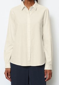 Camisa de botón de manga larga en un tono beige claro con cuello. Tela suave, corte recto y dobladillo curvado. Combínala con pantalones oscuros.
