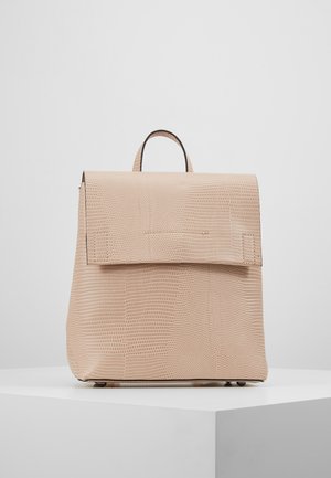Mochila beige con textura, con asa superior y cierre de solapa grande, colocada sobre una plataforma blanca contra un fondo gris claro liso.