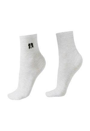 Paire de chaussettes blanches à tige courte, dont une porte une petite broderie d'un visage de chien noir et blanc près du bord.
