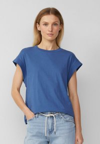 Blaues Baumwoll-T-Shirt mit umgeschlagenen kurzen Ärmeln, rundem Halsausschnitt und lockerer Passform; kombiniert mit hellen Jeans aus Denim mit einem Kordelzug in der Taille.