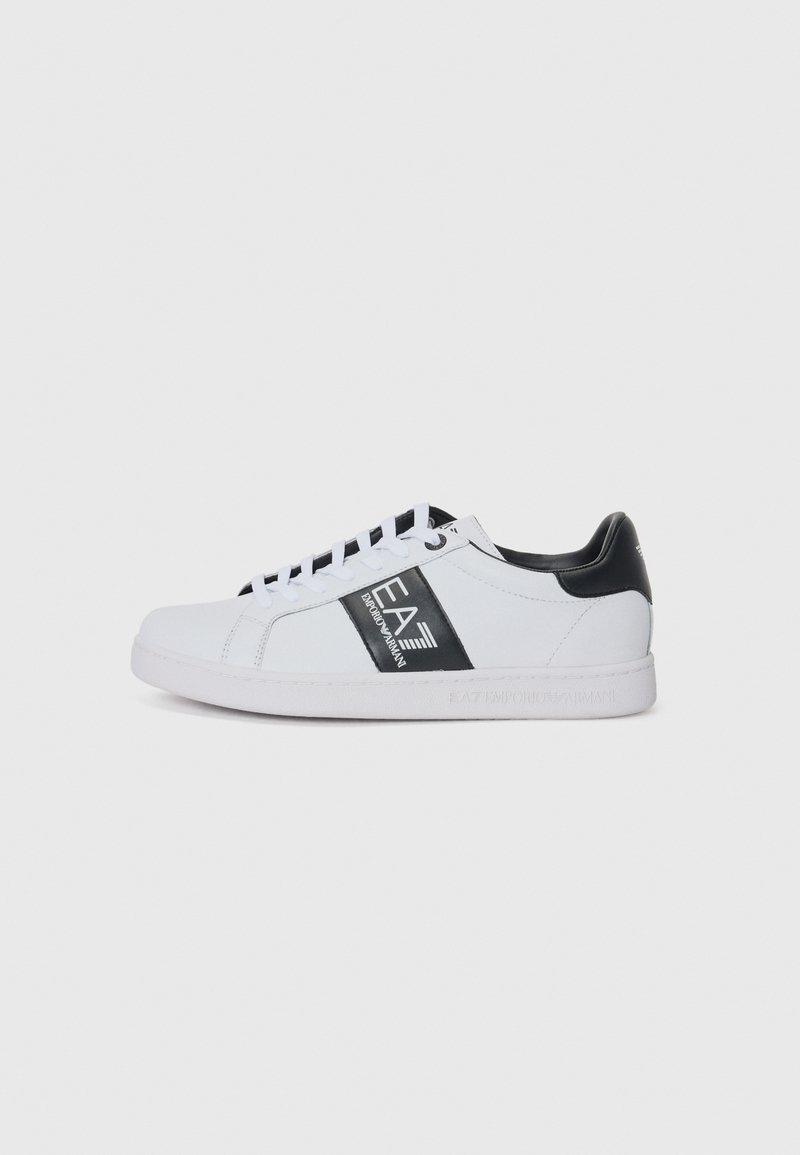Adidași albi cu un accent negru și branding pe lateral, având un design clasic cu șireturi și material sintetic neted.