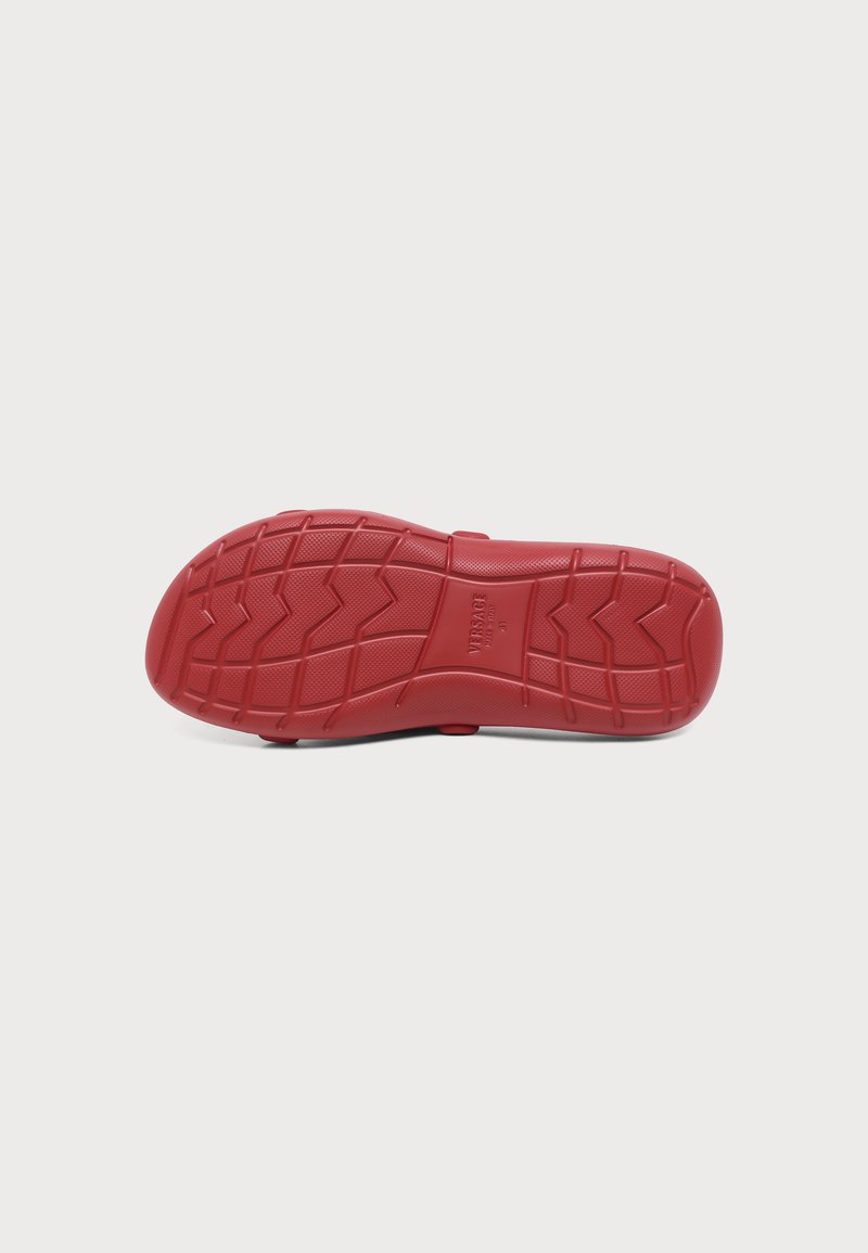 Rote Schuhsohle mit gemustertem Profil und dem Wort Versace, das in der Mitte auf weißem Hintergrund geprägt ist.