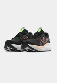 Ténis desportivos pretos com detalhes verdes, apresentando uma parte superior texturizada, sistema de atacadores reforçado e uma entressola branca com sola exterior de borracha preta.