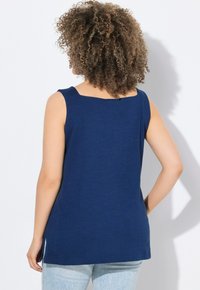 Canotta blu navy in morbido tessuto con scollatura quadrata, senza maniche e spacchi laterali. Vestibilità casual che termina vicino ai fianchi.