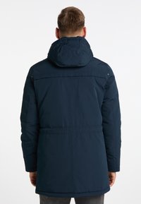 Uomo che indossa un cappotto invernale con cappuccio blu navy, girato di spalle su uno sfondo bianco semplice.