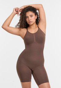 Body marrone con spalline sottili, realizzato in tessuto morbido, caratterizzato da un design aderente e lunghezza fino a metà coscia. Cuciture sottili sul petto.