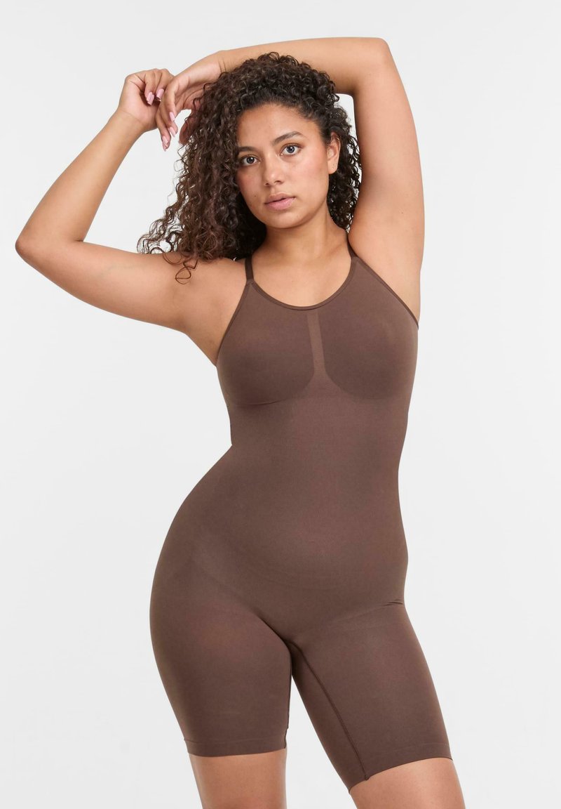 Body marrone con spalline sottili, realizzato in tessuto morbido, caratterizzato da un design aderente e lunghezza fino a metà coscia. Cuciture sottili sul petto.