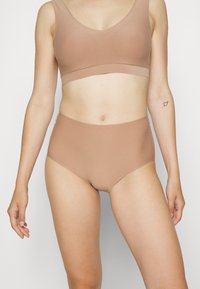 Nahtloser BH und hochgeschnittene Panties aus leichtem, dehnbarem, hellbraunem Stoff. Schlichte Gestaltung mit glatter Textur und ohne sichtbare Beschläge.