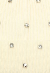 Kremfarget ribbestrikket stoff prydet med ulike sølv rhinestones, som har runde, firkantede og trekantede former, og skaper en teksturert detalj.