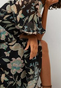 Robe noire à motifs floraux avec un tissu translucide, ornée de motifs floraux bleu clair et rose. Manches fluides, taille cintrée et design en couches.