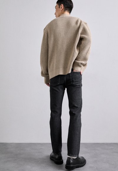 Beige ribbestrikket genser sammen med svarte denimjeans og svarte sko. Genseren har rund hals og en avslappet passform.