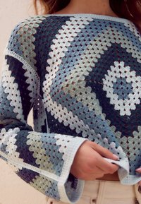 Sweter na szydełku z geometrycznym wzorem w odcieniach niebieskiego, zielonego i białego. Długie rękawy o luźnym kroju i otwartej, siateczkowej strukturze.