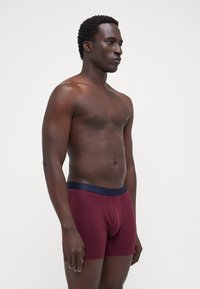 Burgunderfarbene Boxershorts mit einem marineblauen Bund, ausgestattet mit einer glatten Textur, enganliegendem Schnitt und kurzem Beindesign.