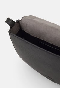 Borsa a tracolla in pelle nera con finitura texturizzata, interno grigio e una piccola maniglia superiore. All'interno presenta scomparti per organizzare gli oggetti.