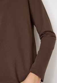 Bruin longsleeve top gemaakt van zachte stof met een gladde textuur, voorzien van een ronde halslijn en een getailleerd ontwerp.