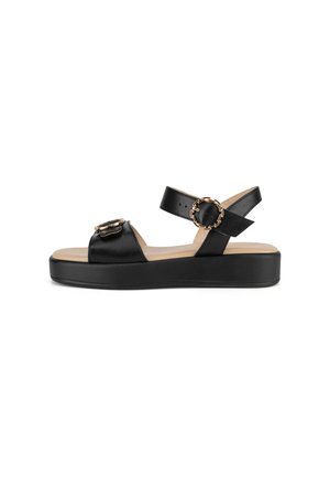 Black platform sandal with two adjustable straps, each featuring a round gold buckle, and a tan footbed.