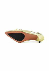 Une chaussure à talon haut jaune pâle à bout pointu vue par en-dessous, avec une semelle noire et marron et un talon fin.