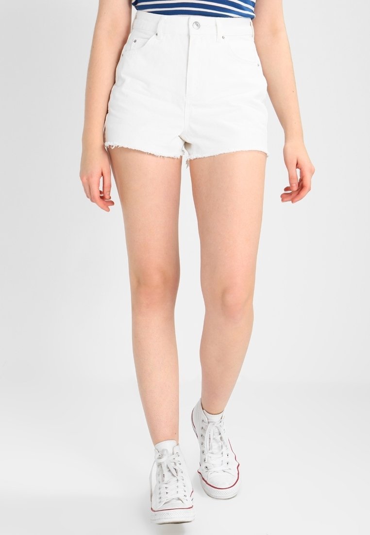 Personne portant un short en jean blanc taille haute avec un ourlet brut, un haut rayé bleu et blanc, et des baskets blanches montantes marchant vers l'avant.