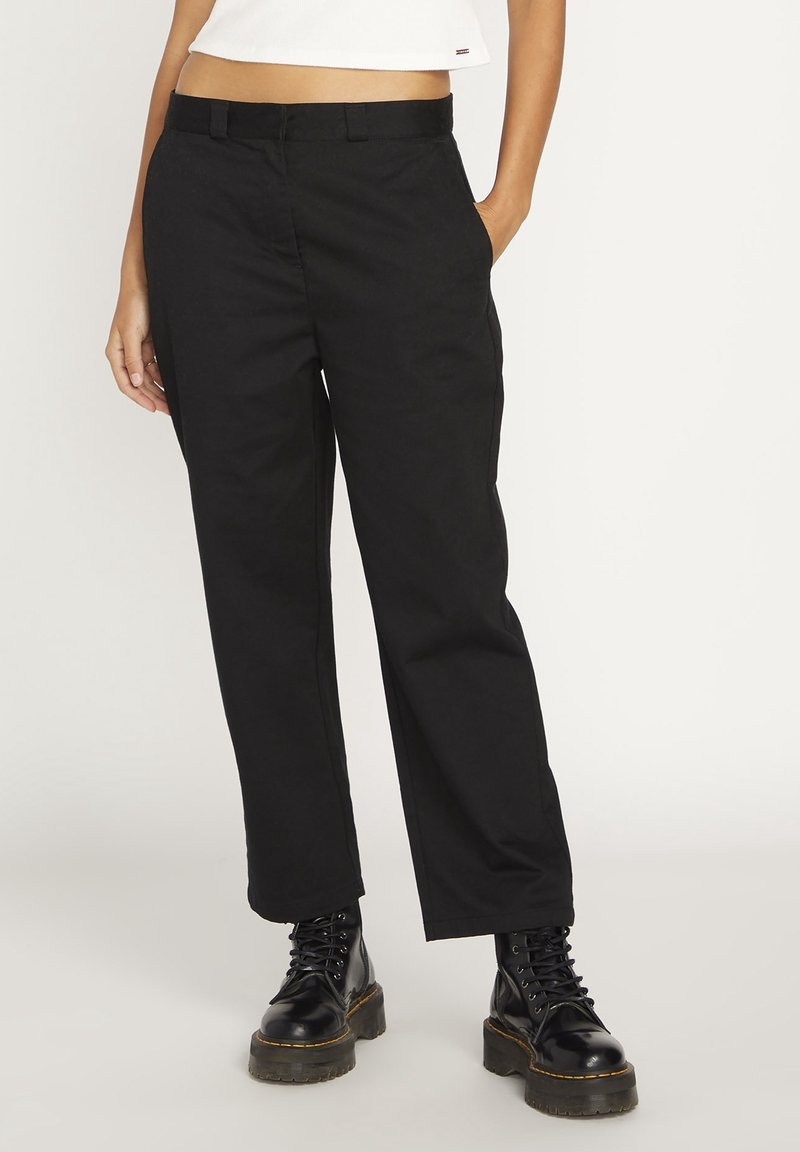 Pantalon en coton noir à coupe droite, avec poches latérales et devant plat. Associé à des bottes noires à lacets pour un contraste.