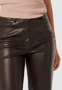 Pantalons en simili cuir noir avec une texture lisse, une coupe ajustée et un design classique à cinq poches. Dotés d'une fermeture éclair et d'un bouton à l'avant.