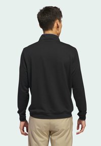 Polo-shirt noir à manches longues avec col, fabriqué dans un tissu texturé et au fit décontracté. La vue arrière montre un design simple sans embellissements.