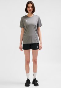 Szara sportowa koszulka z krótkim rękawem, zestawiona z czarnymi szortami. Na obu elementach znajduje się logo. Noszona z białymi skarpetkami i czarnymi trampkami.