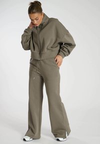 Gekürzter Reißverschluss-Sweatshirt und weit geschnittene Hose in Olivgrün, mit einem strukturierten Stoff, lockerer Passform und dezenten Kordelzugdetails.